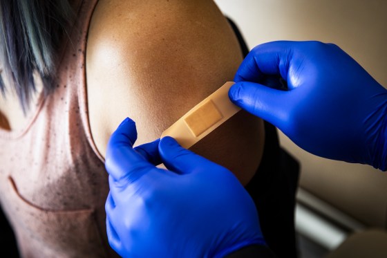Blue gloved hands place a bandaid on someone's arm