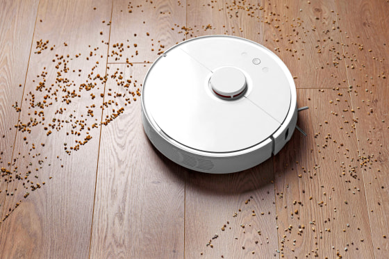 Image: Smart robot vacuum cleaner removes scattered debris from the laminate floor. The concept of a smart home, wireless cleaning of any surfaces