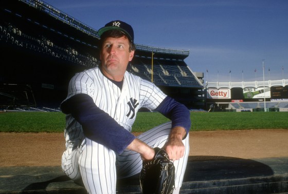 Tommy John sits on the baseball field in uniform, holding a catcher's mitt
