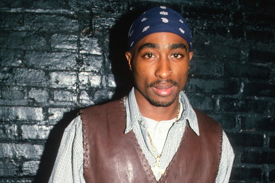 Tupac Shakur stands up again a brick wall painted black