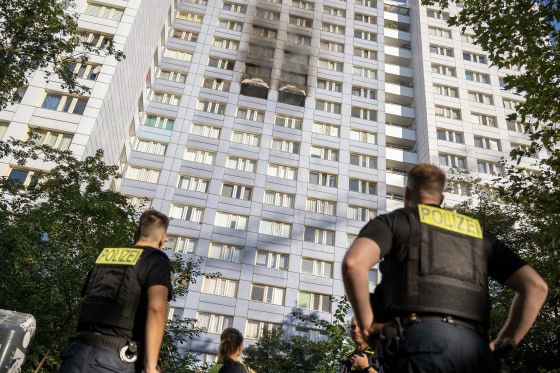 two police officers look up at black smoke coming from the middle of a high-rise apartment building.