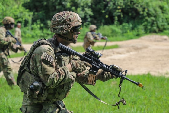 Luke Lem in his army uniform carries a gun while walking in a field