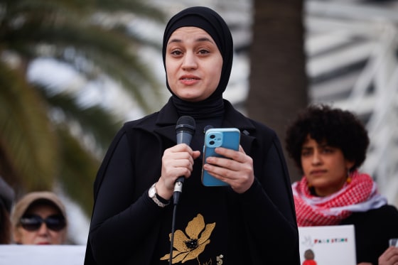 Wissam Hamada speaks into a microphone while standing and hold a cellphone in the other hand