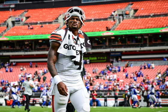 Deshaun Watson walks on the football field in his uniform, with his helmet resting on top of his head