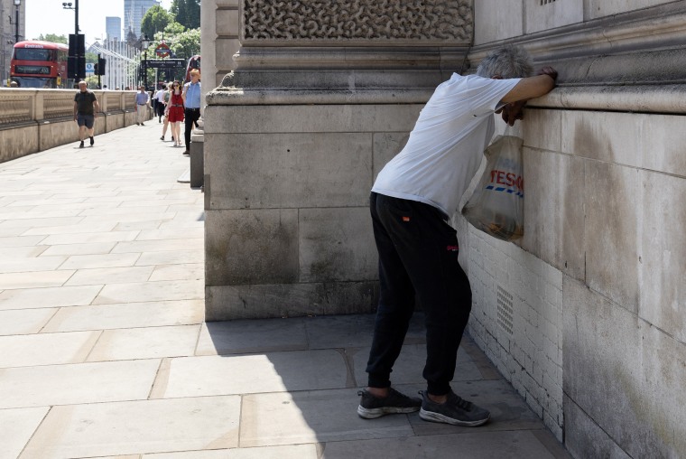 A man resting his head on a concrete ledge in the shade.