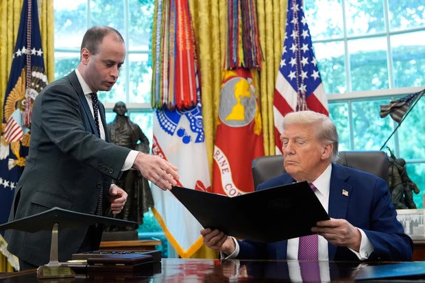 White House staff secretary Will Scharf hands President Trump an executive order to sign in the Oval Office of the White House on Sept. 5, 2025. 