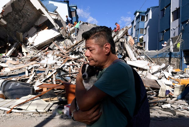 A man carries a dog as he walks past the rubble of a collapsed building after an earthquake in Pereira, Colombia, on Aug. 10, 2026.